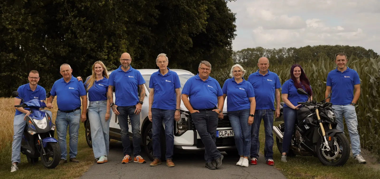 Das Team der Fahrschule Napierski in blauen Poloshirts vor einem Fahrschulauto und Motorrädern